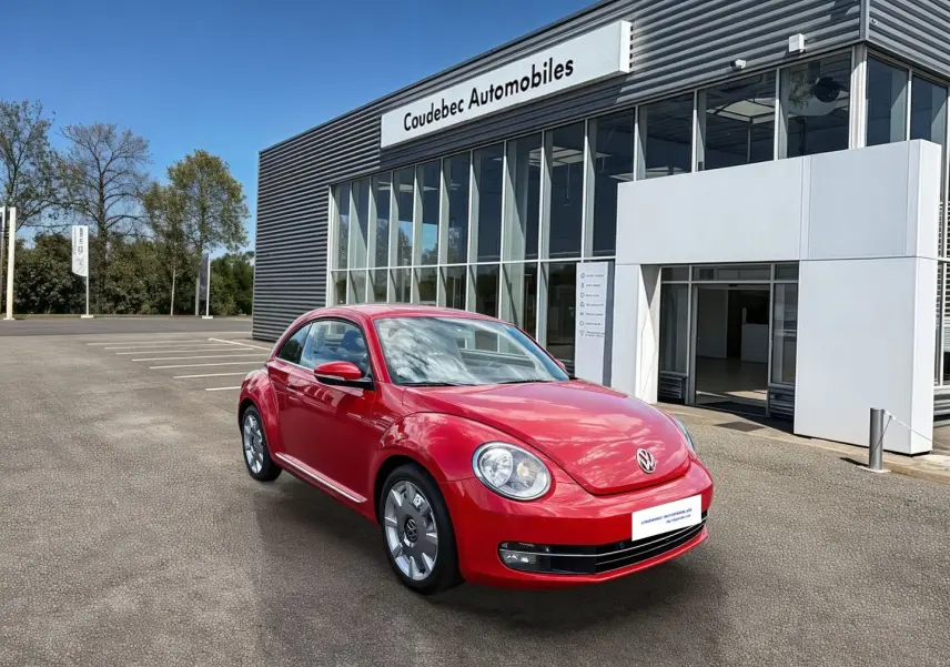 Volkswagen Coccinelle rouge vue 3/4 avant droit, avec jantes 18 pouces, stationnée devant un bâtiment commercial.