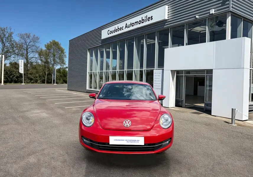 Vue de face d'une Volkswagen Coccinelle rouge Tornade garée devant un bâtiment moderne de concession automobile.