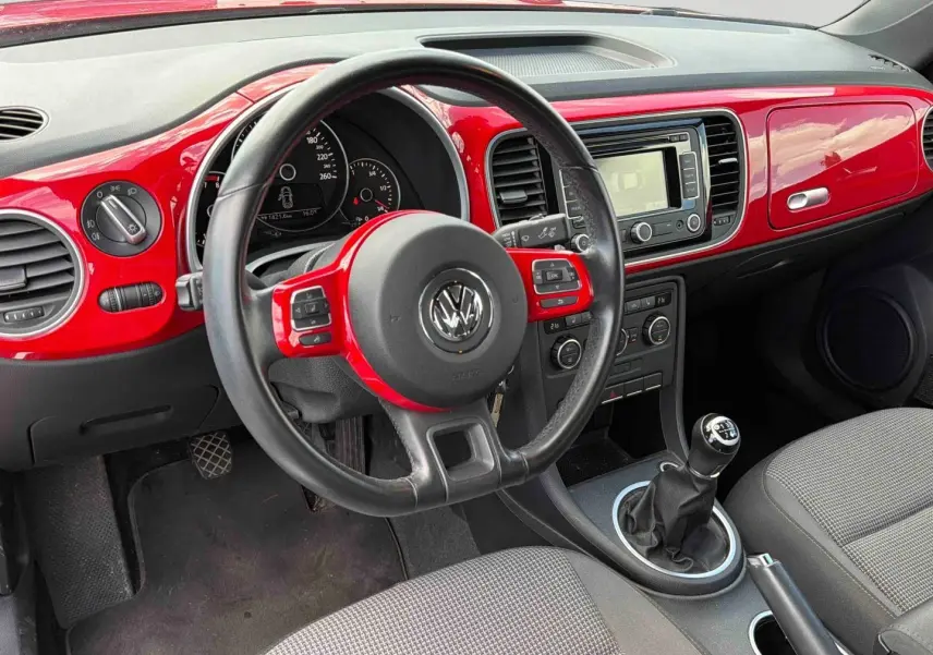 Vue intérieure côté conducteur de la Volkswagen Coccinelle 2012 avec tableau de bord rouge Tornade et volant cuir multifonction.