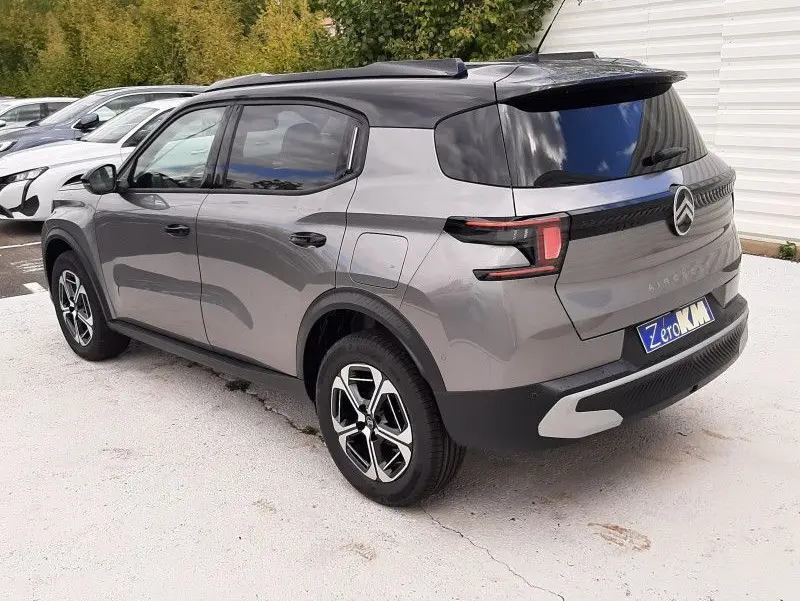 Vue 3/4 arrière gauche d'un Citroën C3 Aircross gris Mercury avec toit noir, jantes modernes et feux arrière LED distinctifs.
