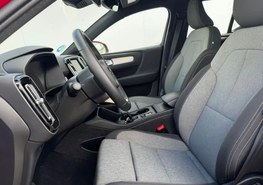 Intérieur avant du Volvo XC40 2024, sièges tissu gris et noir, volant cuir, console centrale avec levier de vitesse.