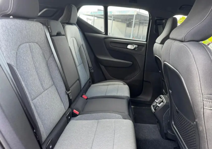 Vue latérale des sièges arrière gris clair et noir du Volvo XC40 2024, avec aérateurs et port USB au centre.