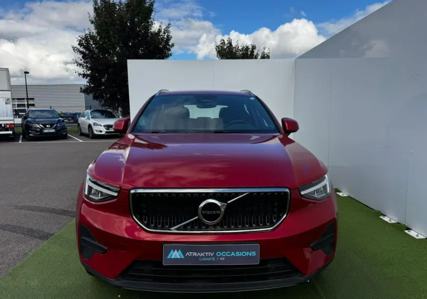 Vue frontale d'un Volvo XC40 Fusion Red Metal 2024 avec calandre noire et détails chromés, sur fond extérieur urbain.