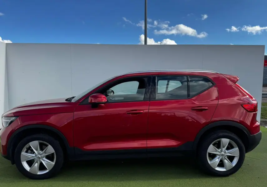 Profil côté gauche du Volvo XC40 2024 en rouge Fusion avec jantes alliage 18 pouces sur fond clair.