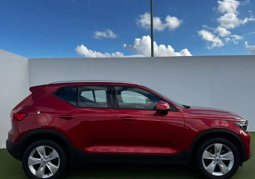 Profil côté gauche du Volvo XC40 2024 en rouge Fusion Metal avec jantes alliage 18 pouces sur fond clair.
