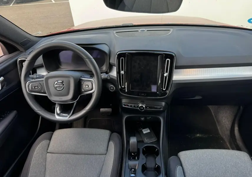 Vue intérieure frontale du tableau de bord et volant cuir du Volvo XC40 2024 avec écran tactile central et sièges gris.