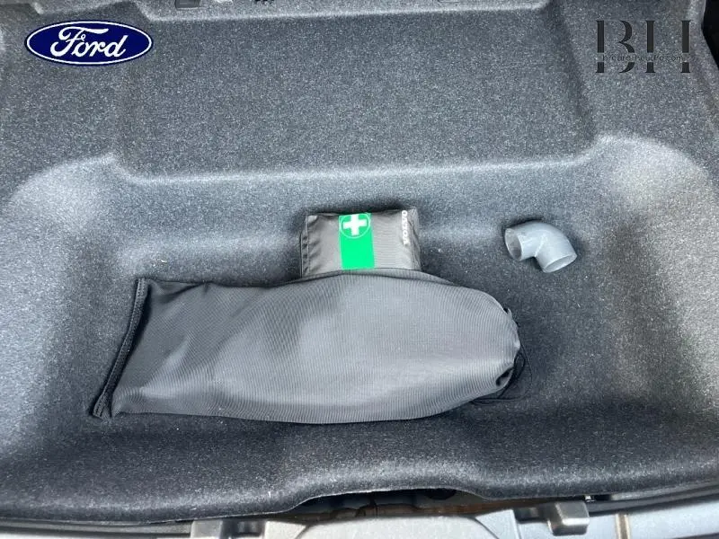 Coffre ouvert d'un Volvo XC40 noir montrant un rangement avec trousse de secours et un tuyau plastique.