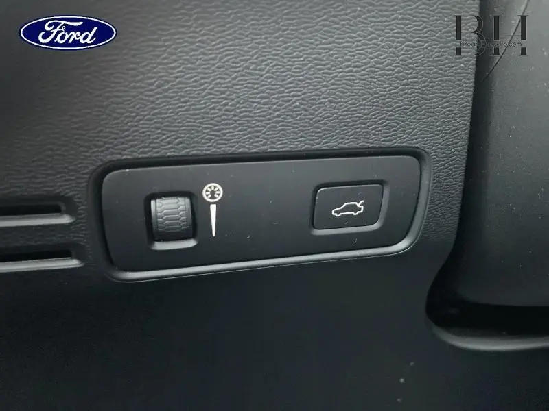 Gros plan sur les commandes noires du tableau de bord du Volvo XC40, avec bouton d'ouverture du coffre et molette de réglage.