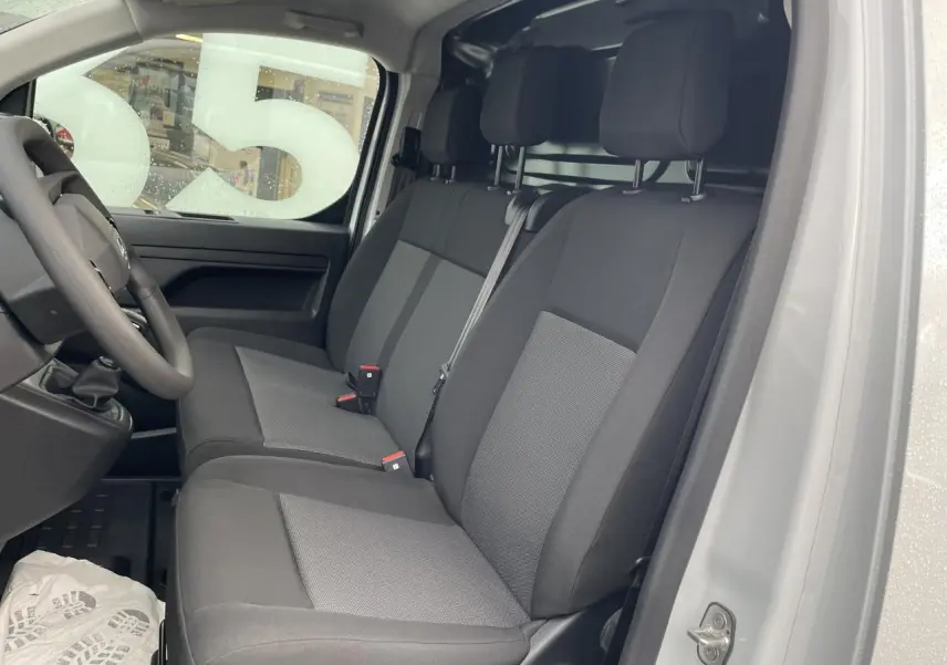 Vue intérieure côté conducteur d’un Opel Vivaro blanc 2024 montrant la banquette passager 2 places en tissu bi-ton noir et gris.