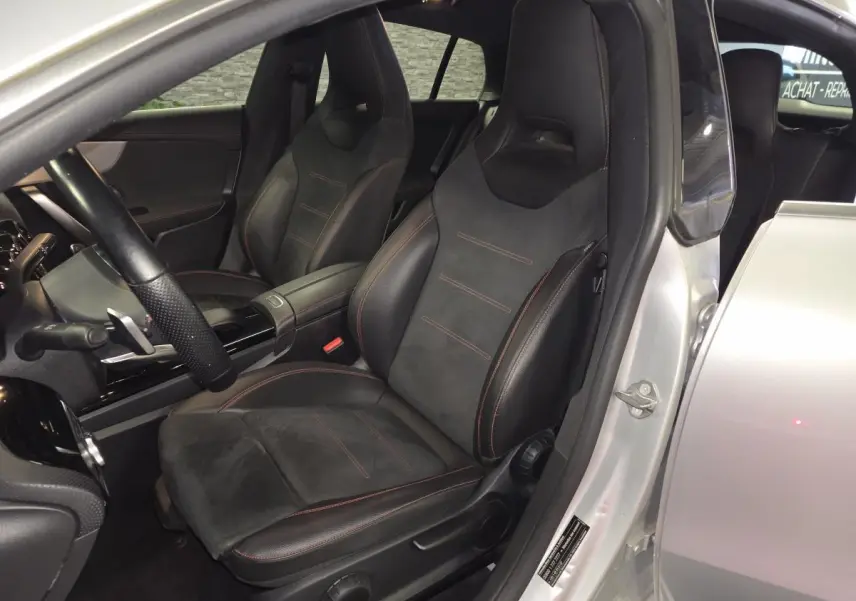 Vue intérieure côté conducteur d'une Mercedes Classe CLA Shooting Brake gris avec sièges sport noirs à surpiqûres rouges.