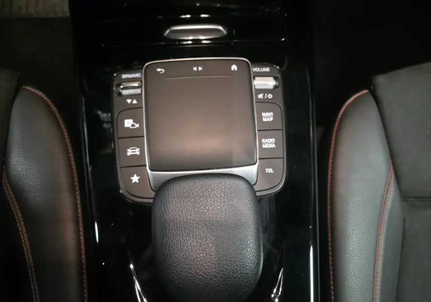 Vue rapprochée de la console centrale noire avec pavé tactile et pommeau de boîte surpiqué rouge du Mercedes CLA Shooting Brake gris.