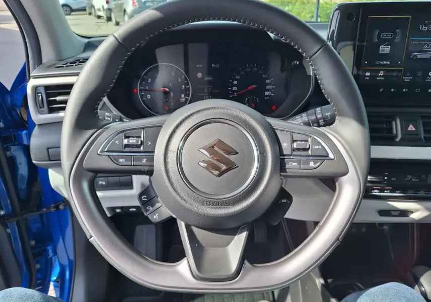 Vue centrée sur le volant noir de la Suzuki Swift bleu 2025, avec tableau de bord et écran tactile visibles.
