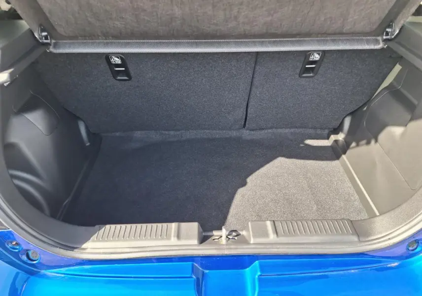 Coffre ouvert vu de l'arrière d'une Suzuki Swift 2025 bleu, montrant l'espace de chargement vide et la garniture intérieure.