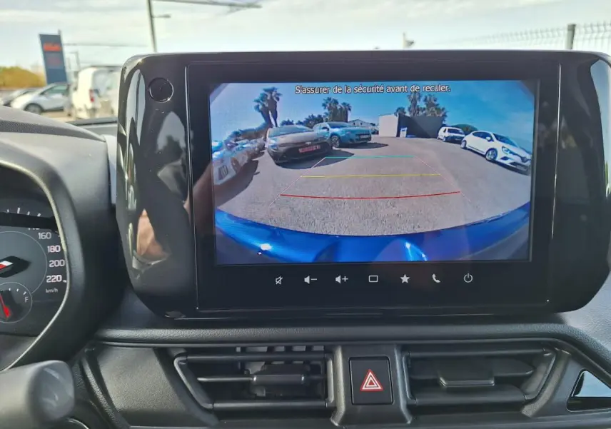 Vue intérieure du tableau de bord d'une Suzuki Swift 2025 avec écran tactile affichant la caméra de recul et le capot bleu visible.