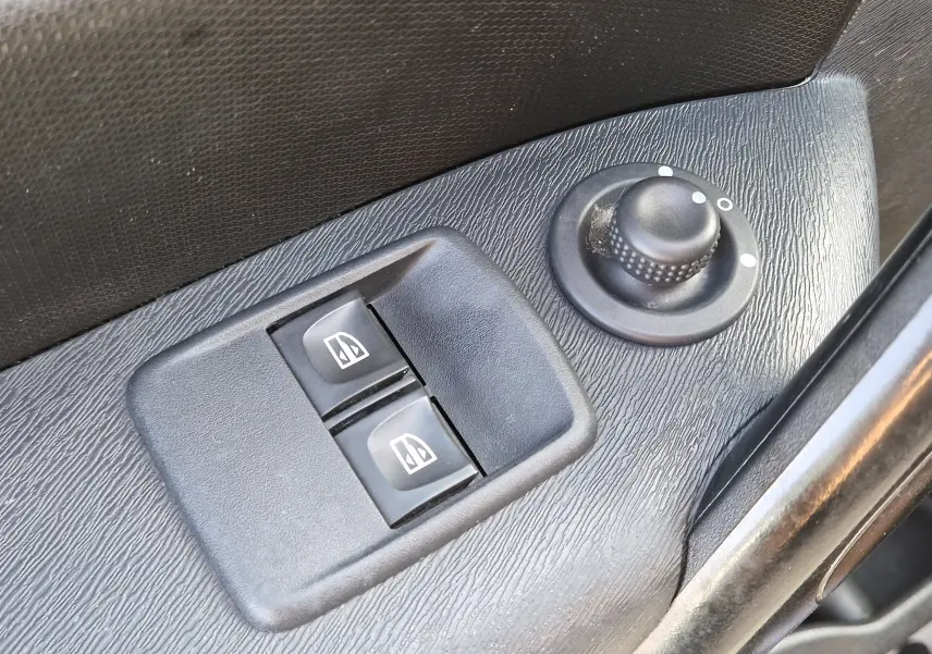 Gros plan sur les commandes électriques des vitres et le réglage des rétroviseurs côté conducteur d’un Renault Kangoo blanc.