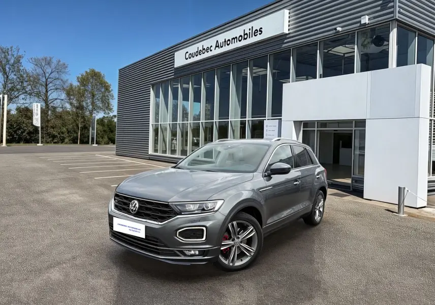 Volkswagen T-Roc gris Indium métal en 3/4 avant droit, avec jantes alliage et calandre R-Line visible.