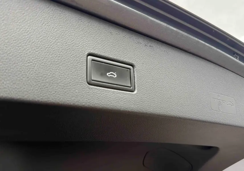 Gros plan sur le bouton d'ouverture électrique du coffre du Volkswagen T-Roc gris Indium, intérieur du hayon visible.