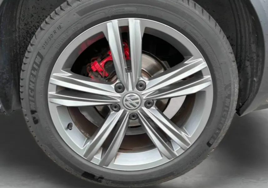Gros plan sur la jante alliage 18 pouces Nevada argentée avec logo Volkswagen et étrier de frein rouge du T-Roc gris Indium.
