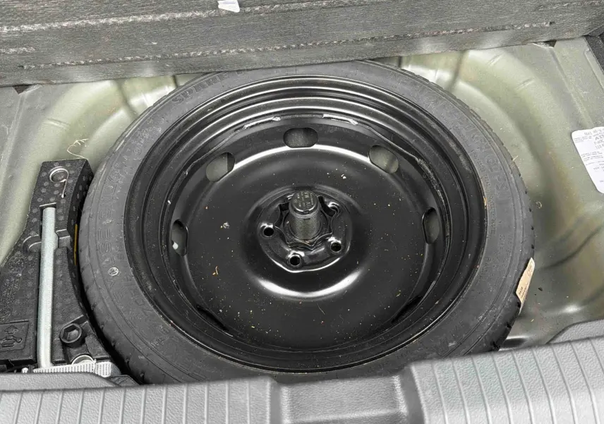 Vue plongeante sur la roue de secours noire et les outils dans le coffre du Volkswagen T-Roc gris Indium Metal.