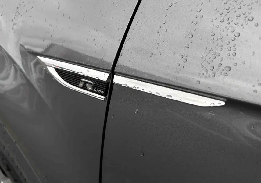 Gros plan sur l’aile avant gauche gris Indium métallisé du Volkswagen T-Roc avec logo R-Line et gouttes de pluie.