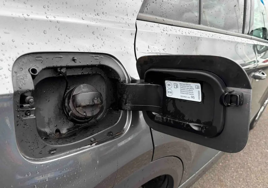 Vue rapprochée du volet de remplissage essence ouvert côté gauche d’un Volkswagen T-Roc gris Indium Metal sous la pluie.