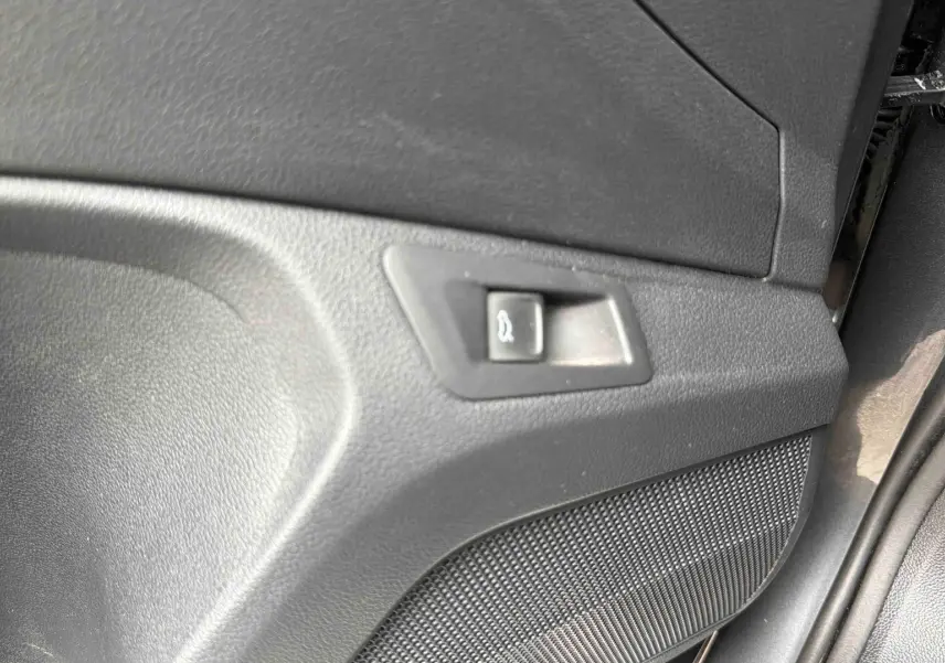 Détail du panneau intérieur de porte avec bouton d'ouverture du coffre sur Volkswagen T-Roc gris Indium.