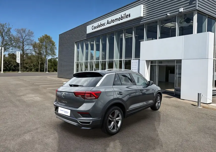 Volkswagen T-Roc gris Indium métal vu en 3/4 arrière droit devant un concessionnaire Coudebec Automobiles.