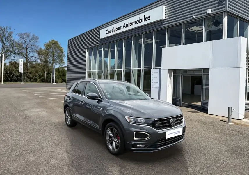 Volkswagen T-Roc gris Indium métal en 3/4 avant droit, avec jantes alliage 18 pouces et détails R-Line visibles.