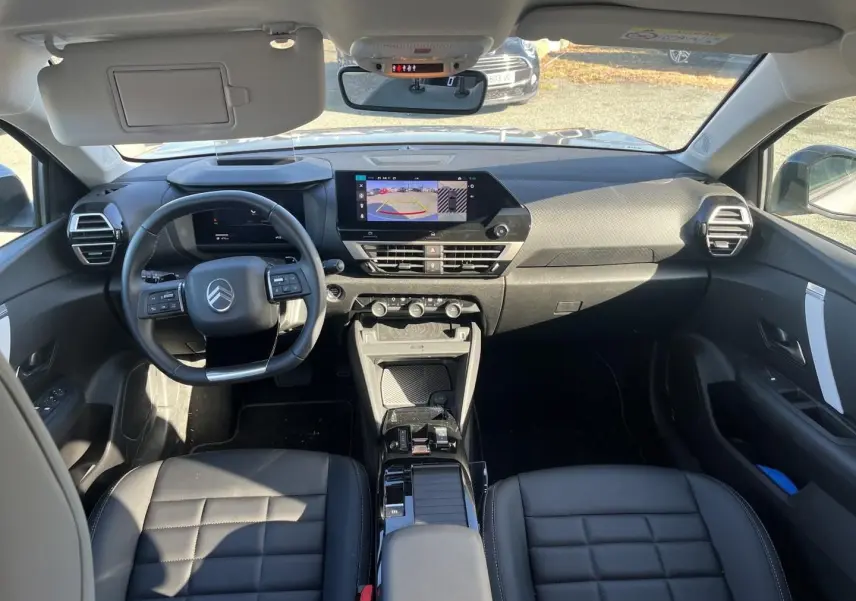 Intérieur Citroën C4 X hybride 2025 vu de face, tableau de bord moderne avec écran tactile et sièges cuir noirs.