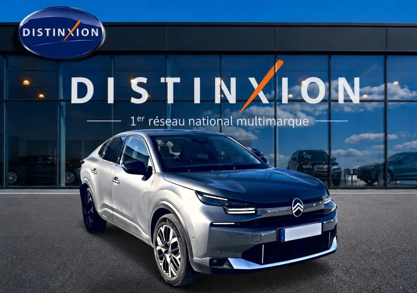 Citroën C4 X gris mercure vue 3/4 avant droit, avec calandre distinctive et jantes alu devant un showroom Distinxion.