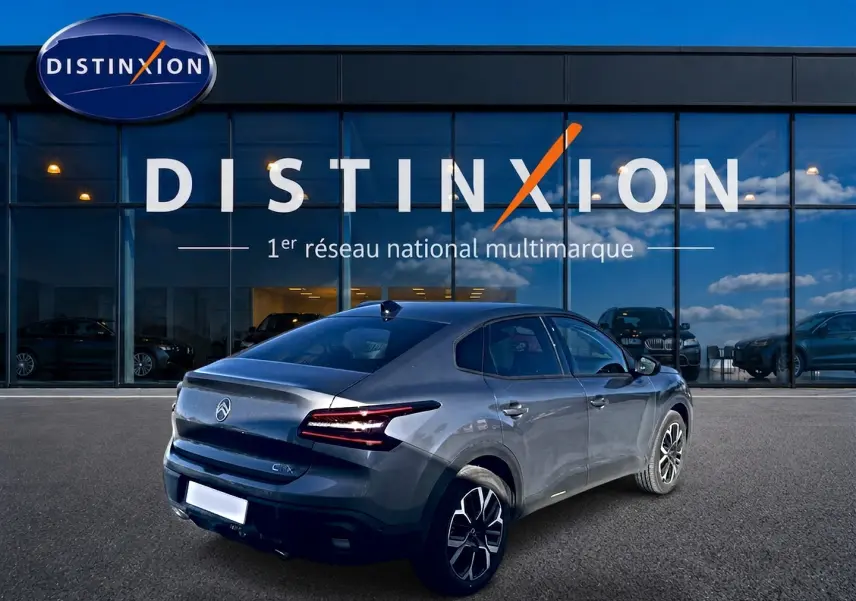 Vue 3/4 arrière droite d'une Citroën C4 X gris mercure avec feux arrière LED et jantes alu devant un showroom Distinxion.