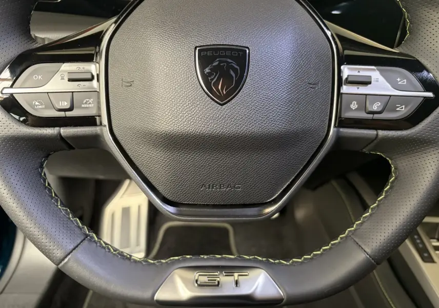 Gros plan sur le volant cuir perforé noir avec logo Peugeot et badge GT, intérieur Peugeot 308 hybride 2025.
