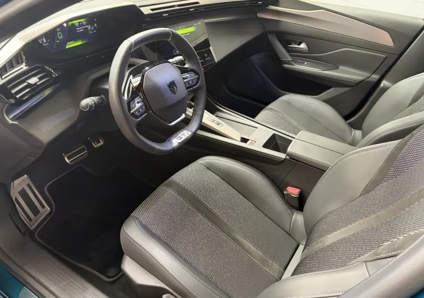 Vue intérieure côté conducteur de la Peugeot 308 GT 2025, avec volant cuir multifonctions et sièges tissu/cuir gris.