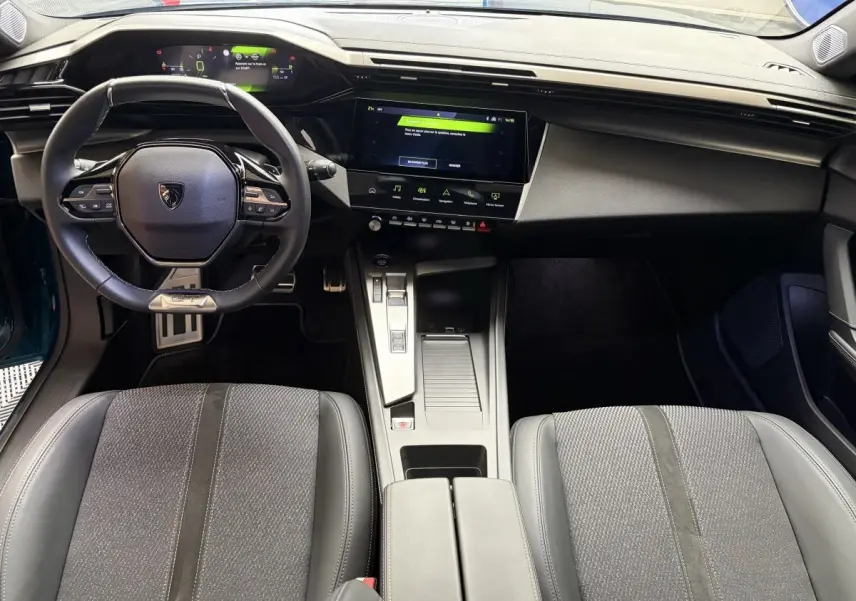 Intérieur de la Peugeot 308 hybride 2025, vue de dessus sur le tableau de bord et volant cuir noir avec écran tactile central.