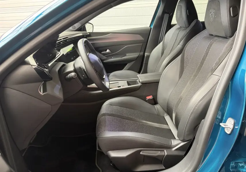 Intérieur avant droit de la Peugeot 308 bleu 2025, sièges cuir noirs avec logo Peugeot brodé sur appuie-tête.