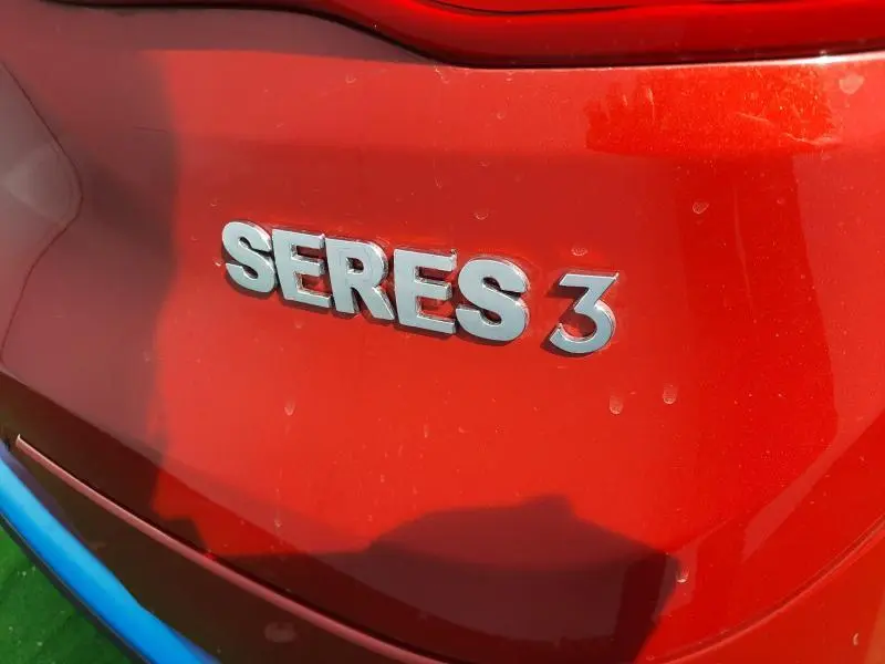 Gros plan sur l'emblème "SERES 3" argenté sur la carrosserie rouge carmin arrière du véhicule électrique.
