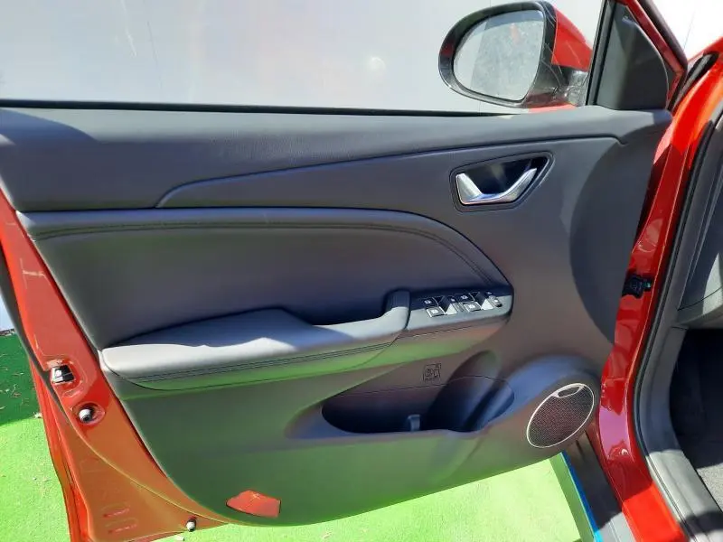 Porte avant gauche ouverte d'une SERES 3 rouge carmin, montrant les commandes électriques et haut-parleur intégré.