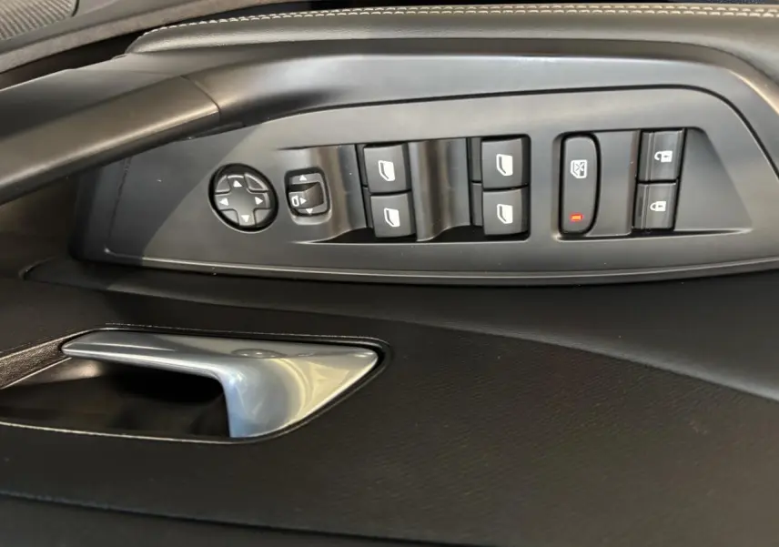 Vue rapprochée des commandes de lève-vitres et rétroviseurs côté conducteur sur porte intérieure noire d’une Peugeot 308 SW gris clair.