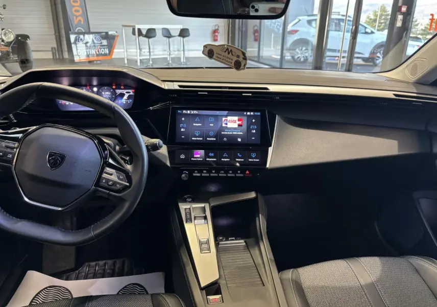 Vue intérieure avant de la Peugeot 308 SW 2024, tableau de bord moderne avec écran tactile central et volant cuir noir.