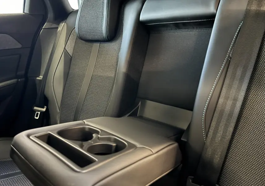 Détail de l'accoudoir central arrière avec porte-gobelets sur la banquette tissu noir de la Peugeot 308 SW 2024.