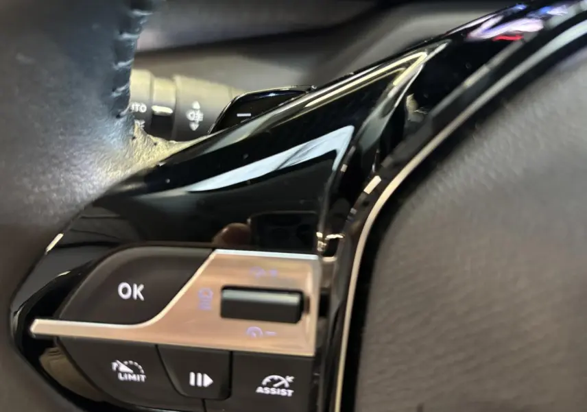 Gros plan sur les commandes au volant noir brillant de la Peugeot 308 SW 2024, avec boutons multifonctions éclairés.