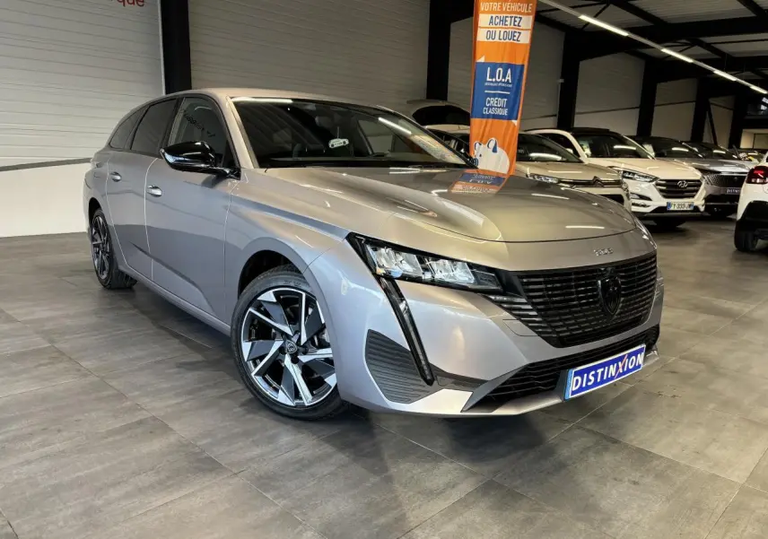 Peugeot 308 SW gris clair métallisé vue 3/4 avant droit en intérieur avec jantes alliage et calandre noire.