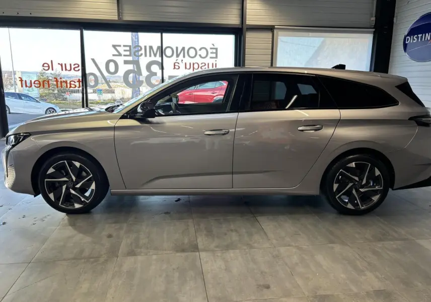Profil droit d'une Peugeot 308 SW gris clair métallisé, avec jantes alliage noires et toit noir en showroom.