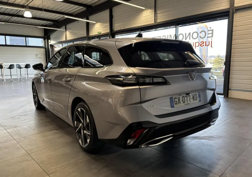 Vue 3/4 arrière droite d'une Peugeot 308 SW gris clair métallisé Artense en intérieur avec jantes alliage 17 pouces.