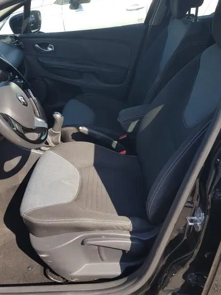 Vue intérieure côté conducteur de la Renault Clio IV noire, siège tissu avec réglage hauteur et volant cuir visible.