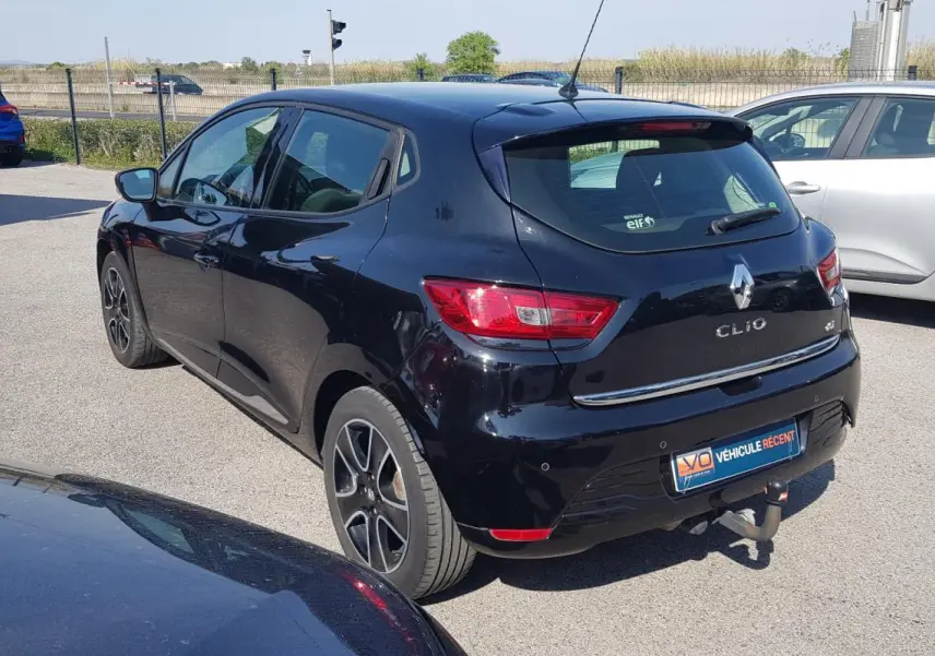 Vue 3/4 arrière droite d'une Renault Clio IV noire avec jantes alliage 16 pouces et attelage visible.