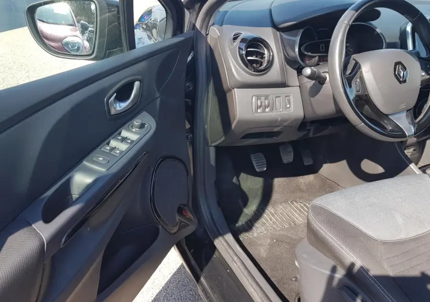 Intérieur côté conducteur d’une Renault Clio IV noire, montrant volant cuir, commandes porte et siège tissu gris.