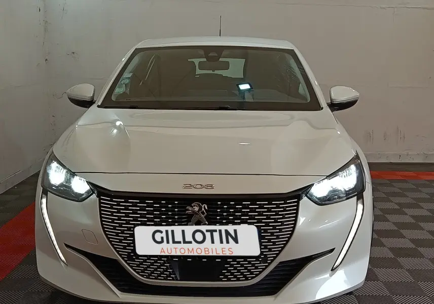 Vue frontale d'une Peugeot 208 électrique Active Business blanche avec phares LED allumés et calandre distinctive.