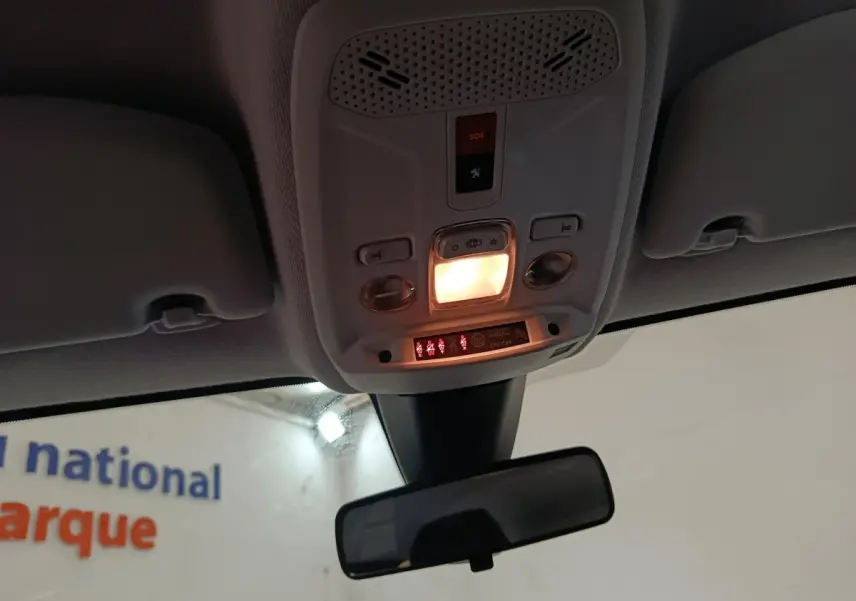 Vue intérieure du plafonnier allumé avec commandes et rétroviseur central d'une Peugeot 208 blanche électrique.