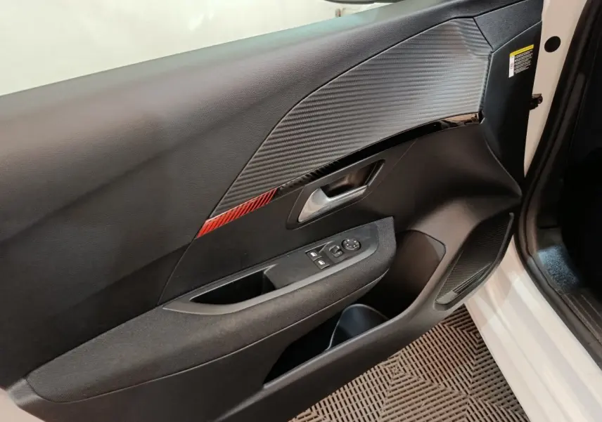 Vue intérieure de la porte avant droite de la Peugeot 208 électrique blanche, avec insert décoratif rouge et commandes électriques.